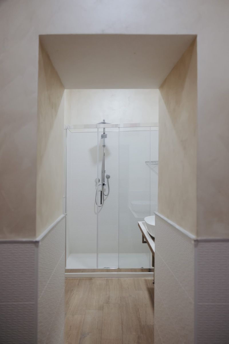 Bagno con box doccia in cristallo, soffione a pioggia e lavabo da appoggio, pareti in resina color sabbia