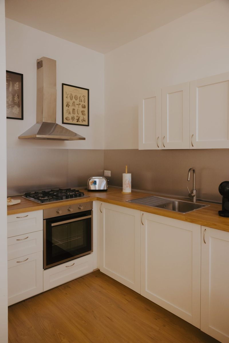 Cucina a elle con anta bianca a telaio, piano di lavoro in legno, piastra a gas, forno e lavello in acciaio