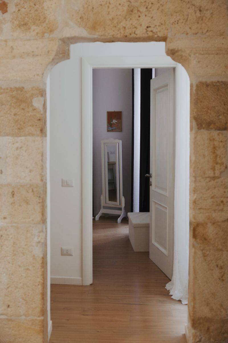 Portale ad arco bianco che dalla zona giorno introduce alla camera, con il pavimento in rovere e lo specchio a bilico in fondo